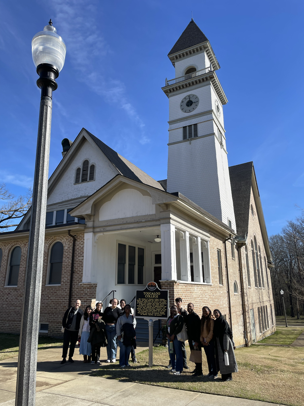 group stands in front of Tougaloo building and sign