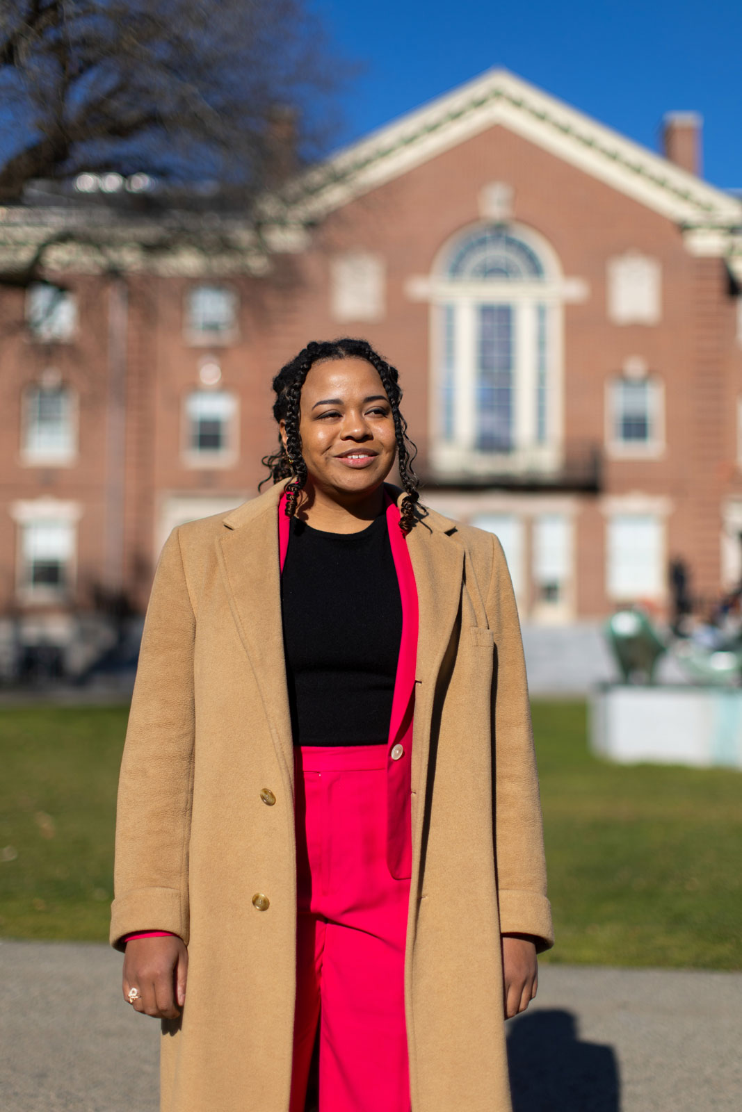 Imani Stewart wears a red suit and tan overcoat on Brown's campus