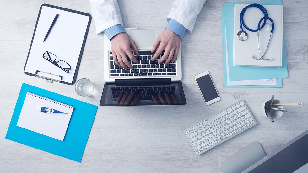 Doctor at desk, typing on laptop