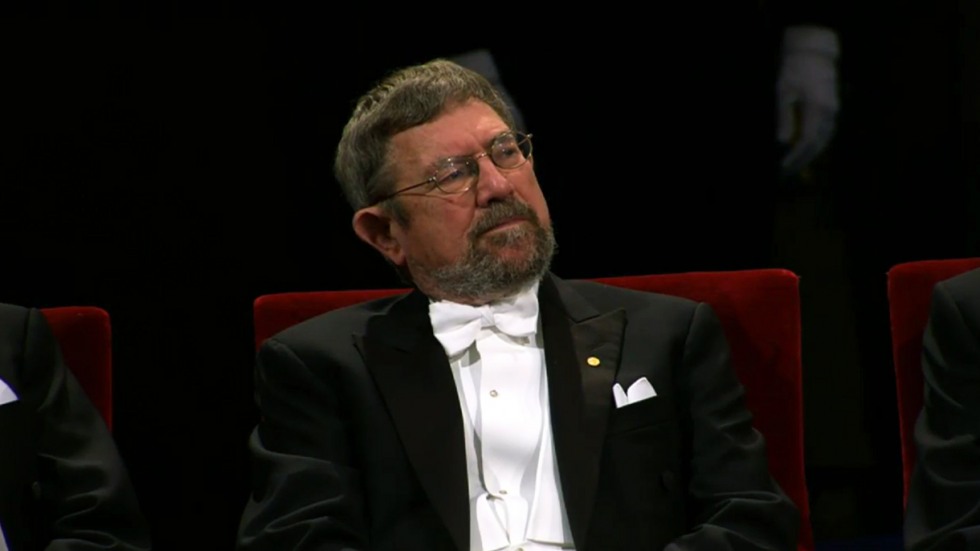 Kosterlitz wearing tux, sitting on stage in Stockholm