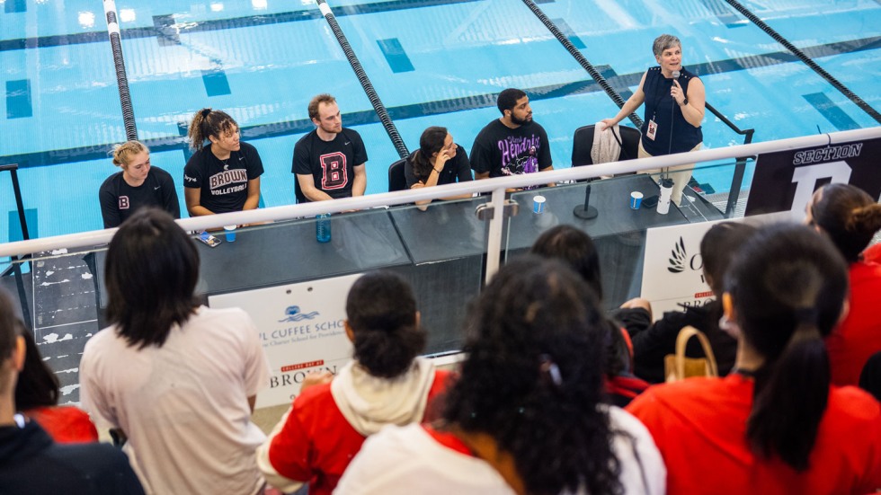 Brown administrators speaking at a table in front of a stadium of students