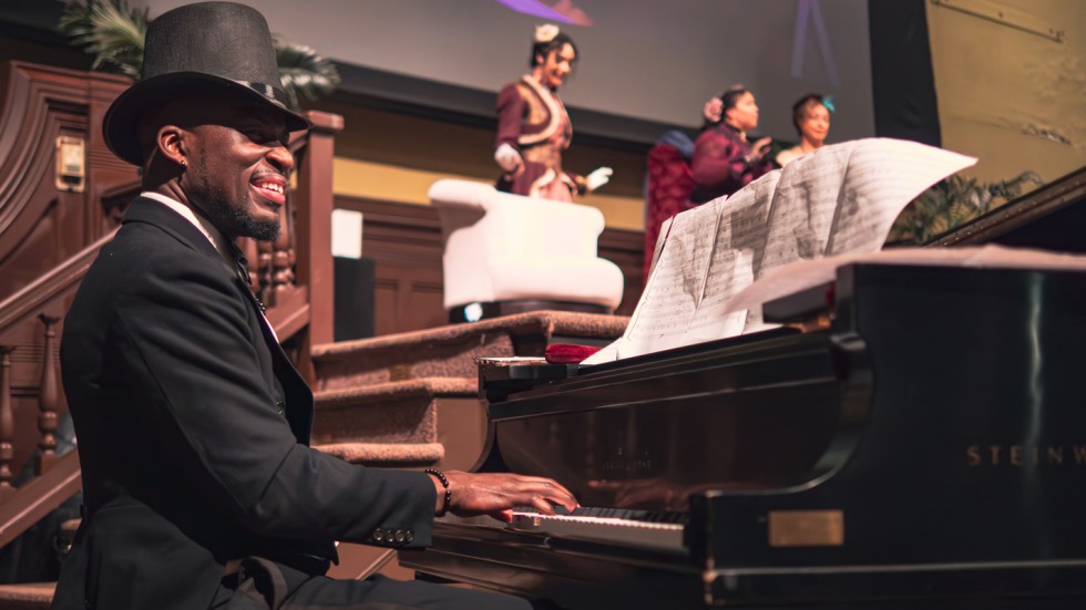 Man in a formal suit and hat plays piano 