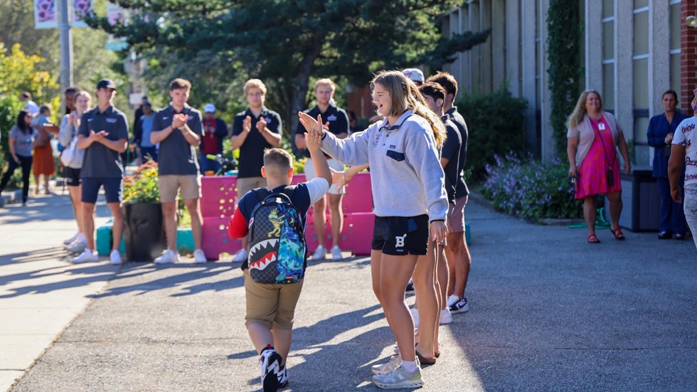 Kids walk into school surrounded by Brown student-athletes cheering them on