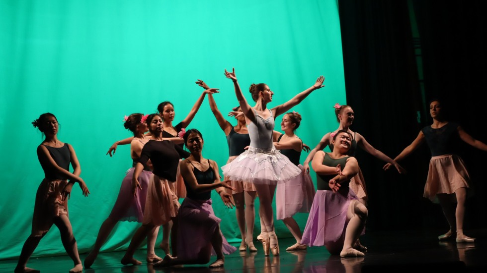 Ballet dancers gather on stage in front of a green curtain