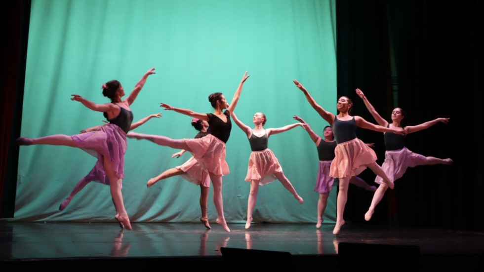 Ballet dancers gather on stage in front of a green curtain